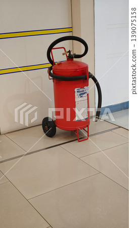 Red fire extinguisher on a metal cart positioned near a wall in a corridor 139075158