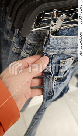 Person holding a pair of jeans while shopping in a clothing store Person holding a pair of jeans while shopping in a clothing store 139075165