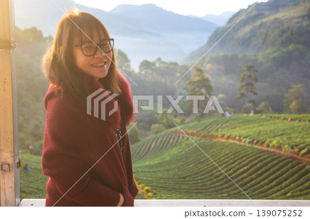 Young woman smiling in a cozy sweater with a beautiful mountain landscape behind her Young woman smiling in a cozy sweater with a beautiful mountain landscape behind her 139075252