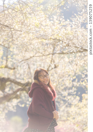 Smiling woman in glasses wearing a maroon hooded jacket with fur trim in spring 139075259
