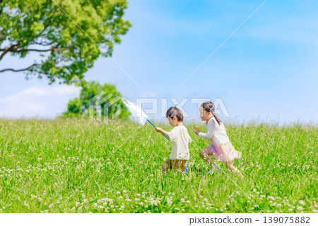 Children running around and playing in a field under a blue sky. Children running around and playing in a field under a blue sky. 139075882