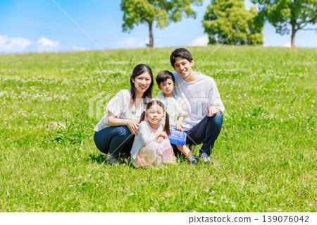 A family sitting on a meadow in the blue sky 139076042