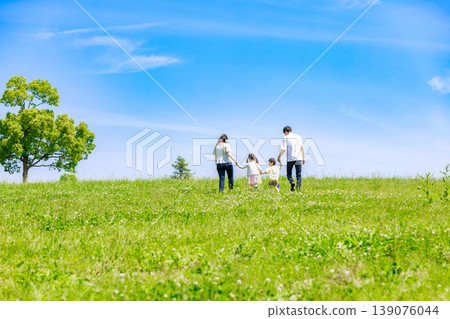 A family walking hand in hand through a meadow under the blue sky A family walking hand in hand through a meadow under the blue sky 139076044