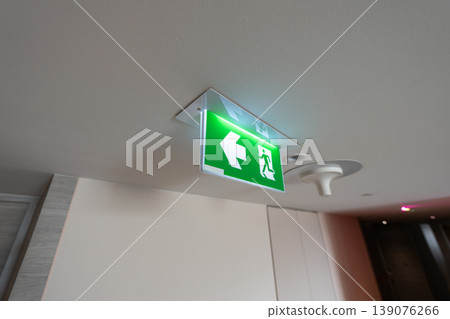 An emergency fire exit light box with arrow hangs from a hospital ceiling, combining evacuation drill concept with clear safety direction and escape guidance. 139076266