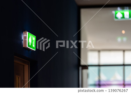 An emergency fire exit light box with arrow hangs from a hospital ceiling, combining evacuation drill concept with clear safety direction and escape guidance. An emergency fire exit light box with arrow hangs from a hospital ceiling, combining evacuation drill concept with clear safety direction and escape guidance. 139076267