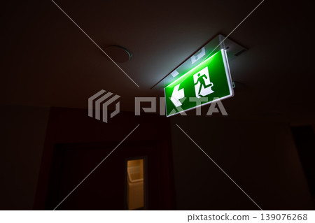 An emergency fire exit light box with arrow hangs from a hospital ceiling, combining evacuation drill concept with clear safety direction and escape guidance. 139076268