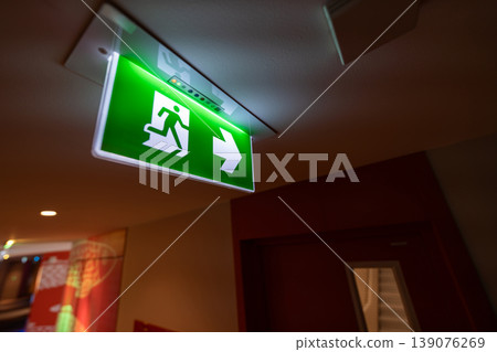 An emergency fire exit light box with arrow hangs from a hospital ceiling, combining evacuation drill concept with clear safety direction and escape guidance. 139076269