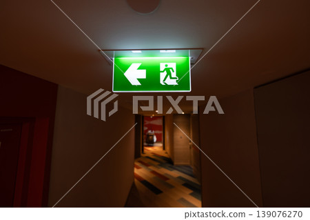 Green emergency exit signs glow above indoor corridors, combining clear direction guidance with fire safety planning and evacuation readiness. Green emergency exit signs glow above indoor corridors, combining clear direction guidance with fire safety planning and evacuation readiness. 139076270