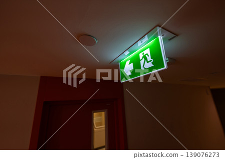 Green emergency exit signs glow above indoor corridors, combining clear direction guidance with fire safety planning and evacuation readiness. Green emergency exit signs glow above indoor corridors, combining clear direction guidance with fire safety planning and evacuation readiness. 139076273