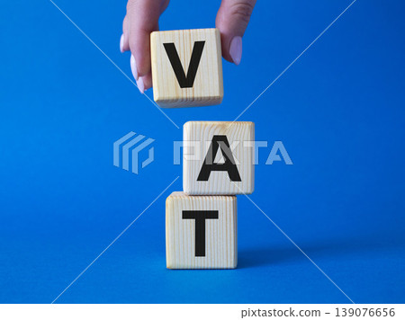 VAT - Value Added Tax symbol. Wooden cubes with word VAT. Businessman hand. Beautiful blue background. Business and Value Added Tax concept. Copy space. VAT - Value Added Tax symbol. Wooden cubes with word VAT. Businessman hand. Beautiful blue background. Business and Value Added Tax concept. Copy space. 139076656