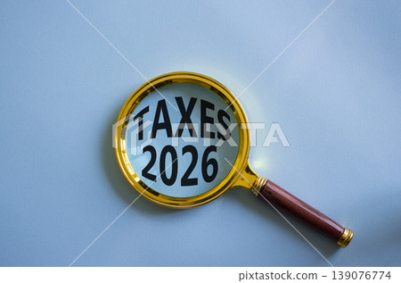 TAXES 2026 symbol. Magnifying Glass with words TAXES 2026. Beautiful blue background. Business and TAXES 2026 concept. Copy space. 139076774