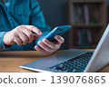 Dual technology work and communication concept, man's hands using smartphone while working on laptop at desk. Online business, multitasking, digital connection, modern professional workspace. 139076865