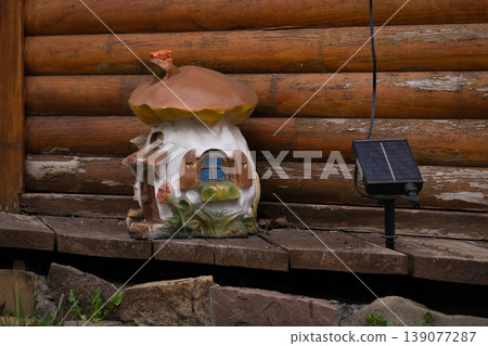 Whimsical mushroom fairy house figurine with solar light against rustic weathered wooden cabin wall background. Whimsical mushroom fairy house figurine with solar light against rustic weathered wooden cabin wall background. 139077287