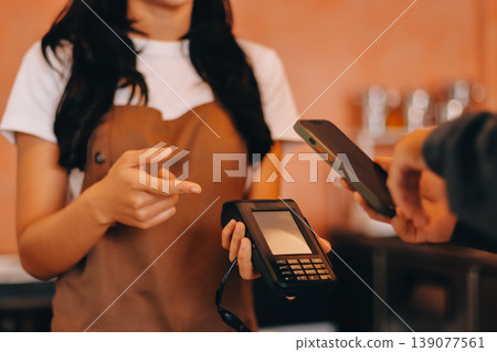 Asian senior female barista adult receiving mobile payment from customer using smartphone at cafe demonstrating modern cashless transaction in cozy local family coffee shop 139077561