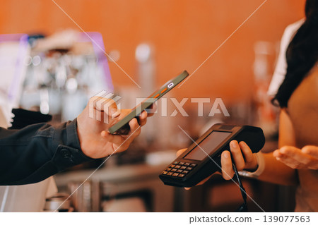 Asian senior female barista adult receiving mobile payment from customer using smartphone at cafe demonstrating modern cashless transaction in cozy local family coffee shop 139077563