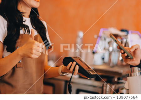 Asian senior female barista adult receiving mobile payment from customer using smartphone at cafe demonstrating modern cashless transaction in cozy local family coffee shop 139077564
