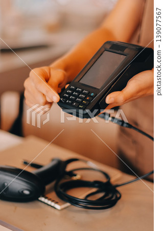 Friendly Asian female barista receives a credit card from a customer for payment. Both women are smiling in a warmly lit coffee shop with a rustic interior. Cashless payments. Small family business 139077567