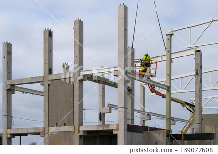 Worker installing steel beam on concrete frame using lift platform at industrial construction site Worker installing steel beam on concrete frame using lift platform at industrial construction site 139077608