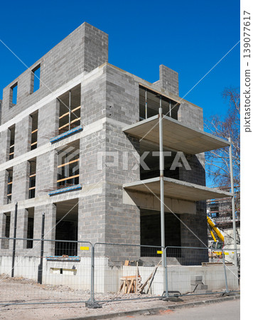 Concrete block residential building under construction with balconies and fenced construction site 139077617