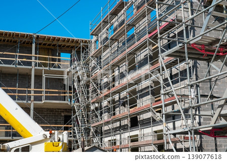 Scaffolding on concrete block building under construction with platforms and structural framework 139077618