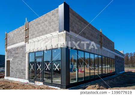 Modern commercial building with glass facade and concrete walls under construction in sunlight Modern commercial building with glass facade and concrete walls under construction in sunlight 139077619