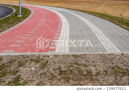 Curved bike path and sidewalk ending at rural edge with tactile paving and red cycling lane Curved bike path and sidewalk ending at rural edge with tactile paving and red cycling lane 139077621