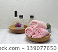 Rolls of clean pink towels with shampoo, conditioner, and soap, alongside a houseplant, on a white table with copy space. 139077650