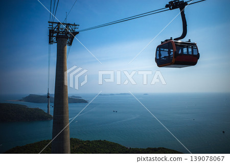 The ropeway's support pillars and orange gondolas stand tall above the blue sea. 139078067