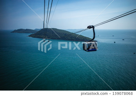 White cable car gondolas crossing over the turquoise blue sea. White cable car gondolas crossing over the turquoise blue sea. 139078068