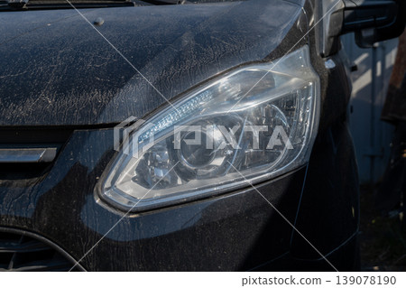 A close view of a car headlight shows dirt on the surface and reflects sunlight. The setting is outdoors with clear daylight and shadows A close view of a car headlight shows dirt on the surface and reflects sunlight. The setting is outdoors with clear daylight and shadows 139078190