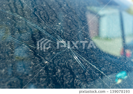 A cracked windshield displays marks caused by a small object on a bright day in a parking lot. The surface shows dirt and debris A cracked windshield displays marks caused by a small object on a bright day in a parking lot. The surface shows dirt and debris 139078193