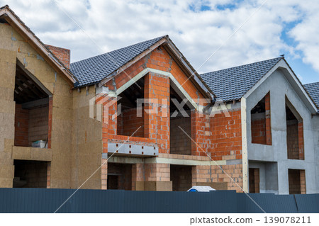Workers build multiple homes with blocks and bricks in a residential neighborhood under a partly cloudy sky Workers build multiple homes with blocks and bricks in a residential neighborhood under a partly cloudy sky 139078211