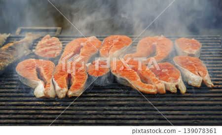 Salmon grill steaks cooking on metal grill with smoke, sliced fish portions, salmon grill process in outdoor kitchen. Seafood cooking, salmon grill service, barbecue preparation, food catering 139078361