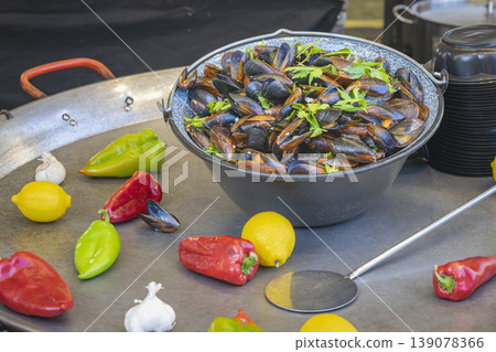 Mussels served in bowl with herbs on metal table with peppers, lemon, garlic. Mussels preparation, fresh ingredients closeup. Seafood cooking, mussels dish, gourmet seafood, fresh market cooking 139078366