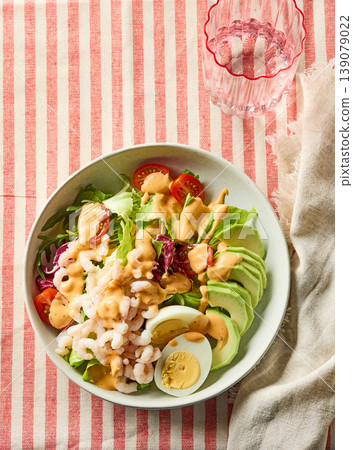 Healthy shrimp avocado salad bowl with egg and dressing  on striped background 139079022
