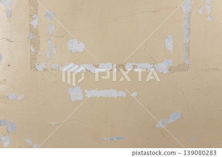 A beige wall with a mixture of adhesive residue and cracks. 139080283
