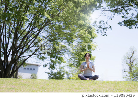 一位女性在藍天綠樹環繞的公園裡練習瑜伽,專注於冥想、健康的生活方式、放鬆和正念。 一位女性在藍天綠樹環繞的公園裡練習瑜伽,專注於冥想、健康的生活方式、放鬆和正念。 139080429