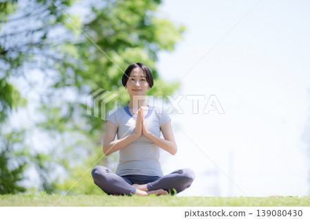 一位女性在綠樹環繞的公園裡練習瑜伽，專注於冥想、健康的生活方式、放鬆和正念。 139080430