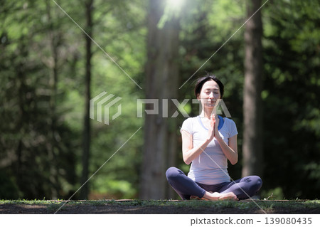 A woman practicing yoga outdoors in a lush green forest, focusing on meditation, a healthy lifestyle, relaxation, and mindfulness. (Hands clasped in prayer) A woman practicing yoga outdoors in a lush green forest, focusing on meditation, a healthy lifestyle, relaxation, and mindfulness. (Hands clasped in prayer) 139080435