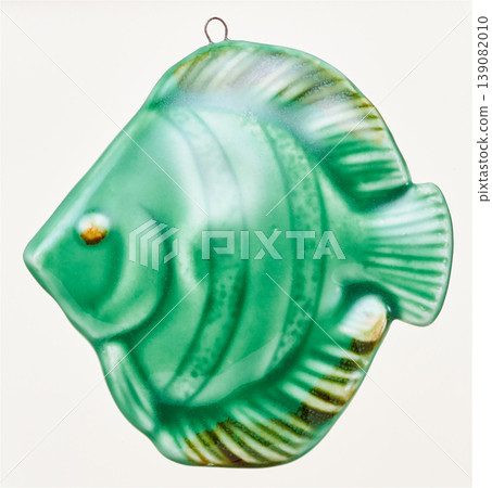 A wall hanging decoration featuring a green ceramic fish cut out against a white background. A wall hanging decoration featuring a green ceramic fish cut out against a white background. 139082010