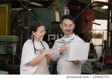 A couple using digital transformation (DX) to check laptops in a factory, showcasing a positive image of growth and success through IT and AI-driven business efficiency. 139082747