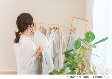 An Asian woman choosing clothes while looking in a full-length mirror (shopping, coordinating outfits, sale, shopping). An Asian woman choosing clothes while looking in a full-length mirror (shopping, coordinating outfits, sale, shopping). 139083325