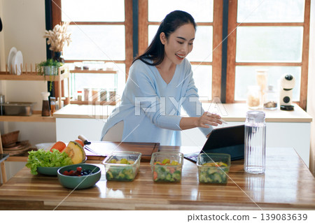 Woman using tablet to follow healthy cooking recipe while preparing fresh meal at home kitchen Woman using tablet to follow healthy cooking recipe while preparing fresh meal at home kitchen 139083639