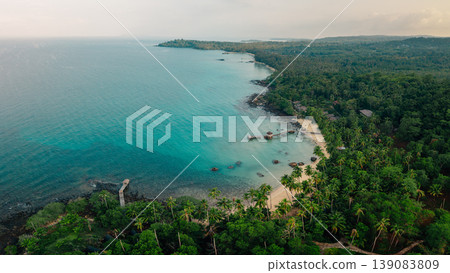 Aerial view of a beautiful tropical island coastline with clear turquoise water, white sand beach, and lush green palm trees. 139083809