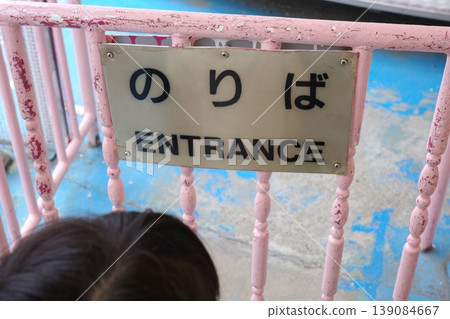 一個孩子在遊樂園遊樂設施入口處排隊等候,旁邊立著一塊雙語標牌,上面寫著「遊樂設施區」。 一個孩子在遊樂園遊樂設施入口處排隊等候,旁邊立著一塊雙語標牌,上面寫著「遊樂設施區」。 139084667