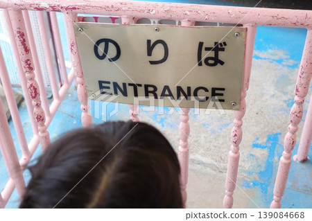一個孩子在遊樂園遊樂設施入口處排隊等候,旁邊立著一塊雙語標牌,上面寫著「遊樂設施區」。 一個孩子在遊樂園遊樂設施入口處排隊等候,旁邊立著一塊雙語標牌,上面寫著「遊樂設施區」。 139084668