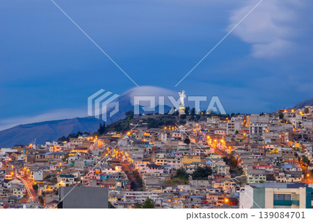 Stunning cityscape of Quito, Ecuador, during the blue hour. The iconic Virgin of El Panecillo rises above the illuminated city, with the majestic Corazon Volcano in the background. 139084701