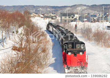 一輛蒸汽機車行駛在北海道白雪皚皚的景色和當地城鎮風光中。 139086282