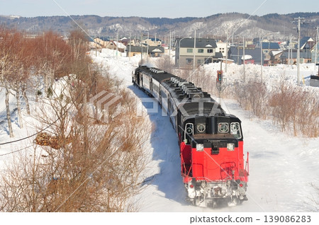 一輛蒸汽機車行駛在北海道白雪皚皚的景色和當地城鎮風光中。 139086283