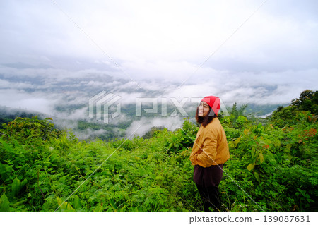 Tourist Asian young woman wearing red hat and yellow jacket standing on peak of mountains and mist in the morning of Thailand Tourist Asian young woman wearing red hat and yellow jacket standing on peak of mountains and mist in the morning of Thailand 139087631